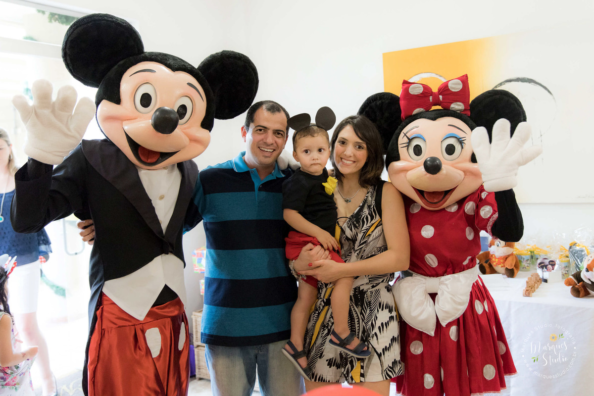 Fotografia tirada no aniversário de 2 aninhos do Guilherme em um Buffeet localizado na Vila Leopoldina - São Paulo, SP. Na foto temos o aniversariante no colo da sua mamãe e do seu lado o papai e dos animadores vestidos de Mickey e Minie. 