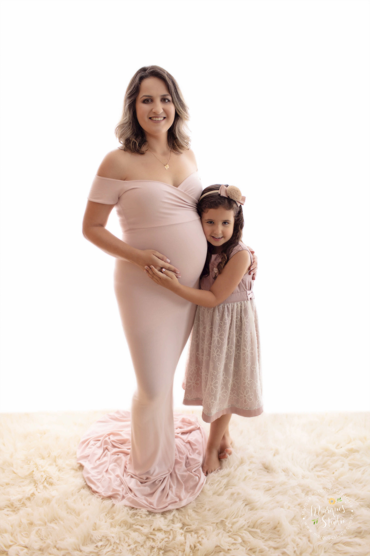 Foto feita no ensaio fotográfico de gestante da Sara. Na foto temos a mamãe com uma mão na barriga e com a outra abraçando a sua filhinha mais velha, que também está  abraçando a barriga. O studio fica localizado na Vila Leopoldina - São Paulo, SP.