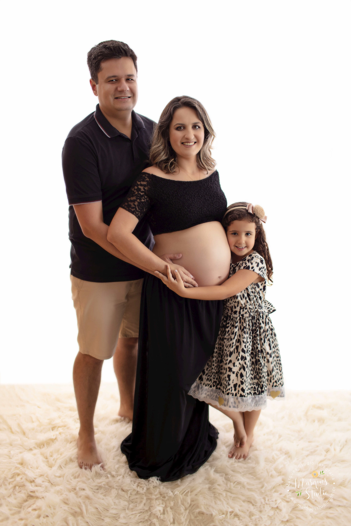 Fotografia feita no ensaio de gestante da Sara. Na foto temos a mamãe com uma mão na barriga, o papai abraçando ela e a sua filhinha mais velha, que também está  abraçando a barriga. O studio fica localizado na Vila Leopoldina - São Paulo, SP.