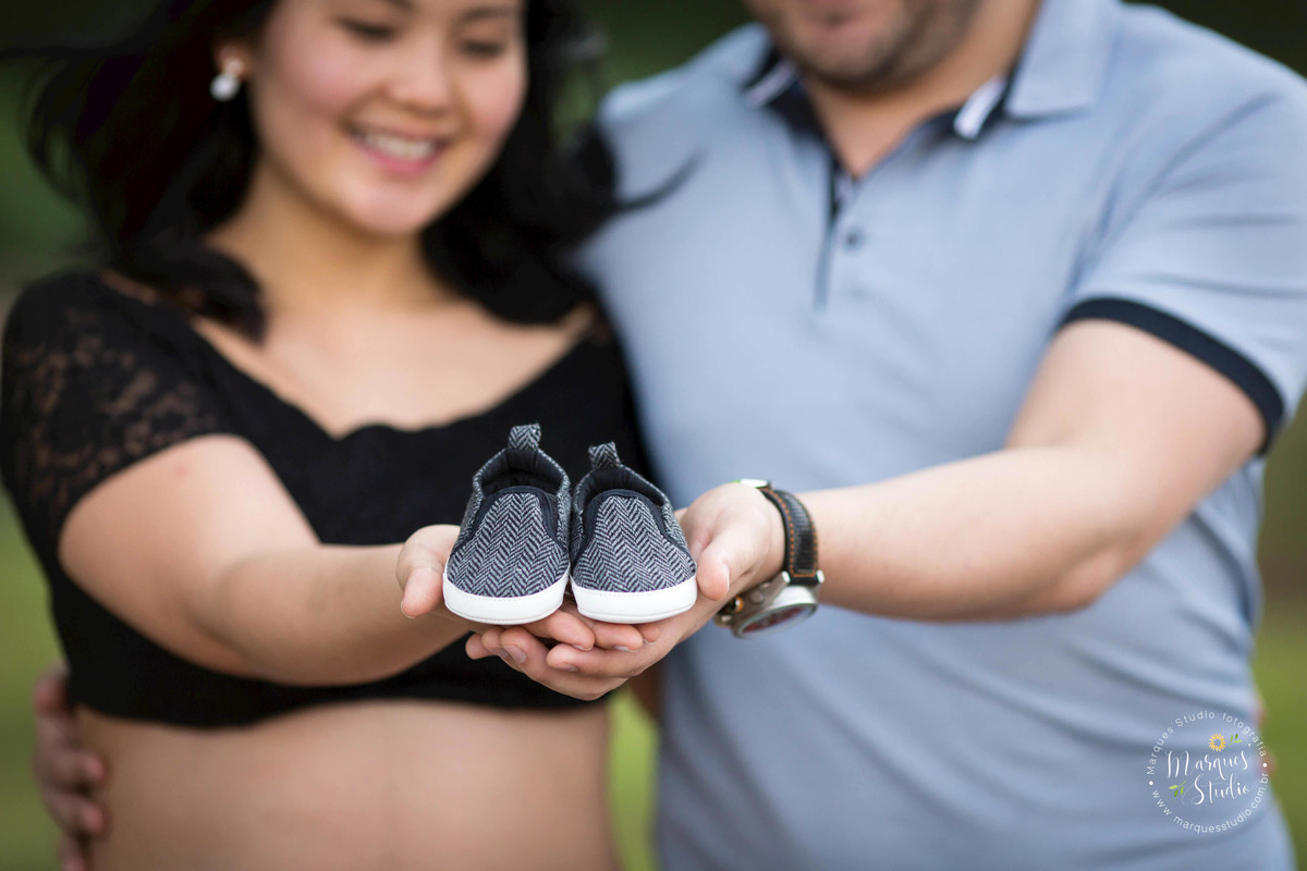 Fotografia registrada em Osasco - São Paulo - SP, no ensaio de gestante da Karla. Na foto temos o papai abraçando a mamãe e juntos estão segurando o sapatinho do seu bebê. O fundo fotográfico é um jardim. A foto foi tirada em Perdizes - São Paulo, SP