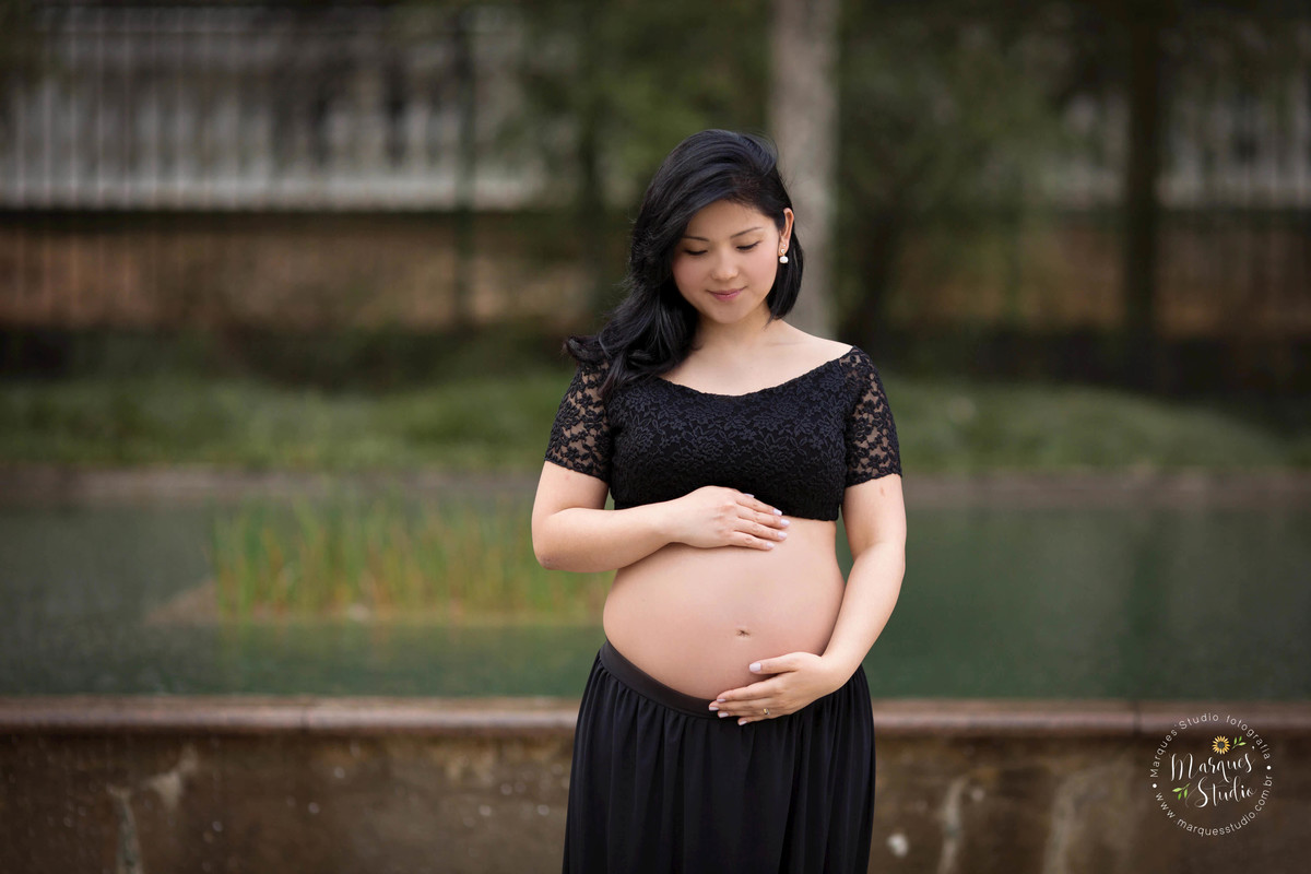 Foto feita no ensaio fotográfico da Karla. Na foto a mamãe está vestida com um lindo conjunto preto de saia e blusa, com as mãos na barriga e olhando para o seu bebê. Foto tirada na Vila Madalena - São Paulo, SP.