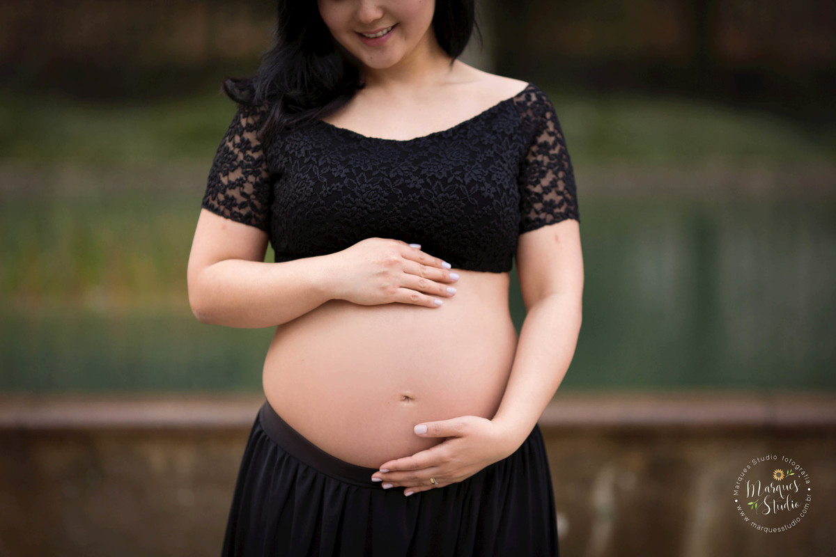 Foto feita no ensaio fotográfico da Karla. Na foto a mamãe está vestida com um lindo conjunto preto de saia e blusa, com as mãos na barriga e olhando para o seu bebê. O foco está na sua barriga.  Foto tirada na Av. Paulista - São Paulo, SP.