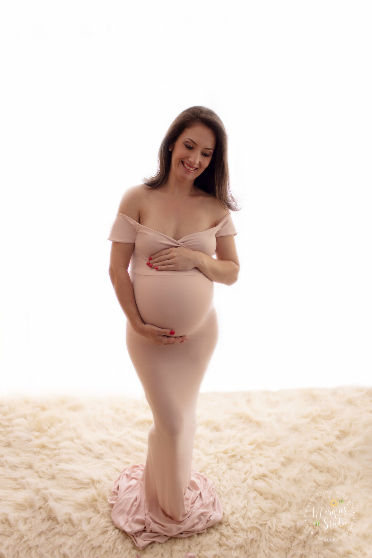 Ensaio de gestante da Eliene em studio localizado no Morumbi - São Paulo, SP. Na foto temos a futura mamãe vestida com um lindo vestido rosa, olhando para a sua bebê na barriga e sorrindo. Suas mãos se encontram sobre a barriga.