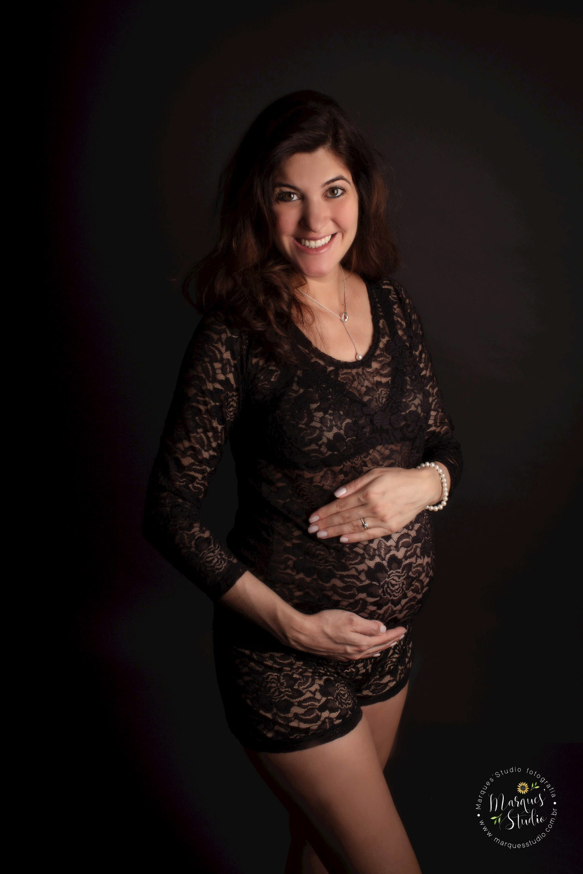 Foto feita no ensaio de gestante da Denise de 32 semanas. Na foto ela está no fundo preto, usando um lindo conjunto preto de renda , sorrindo enquanto segura sua barriga de gestante. A foto foi feita no studio que encontra-se em Perdizes - São Paulo, SP.