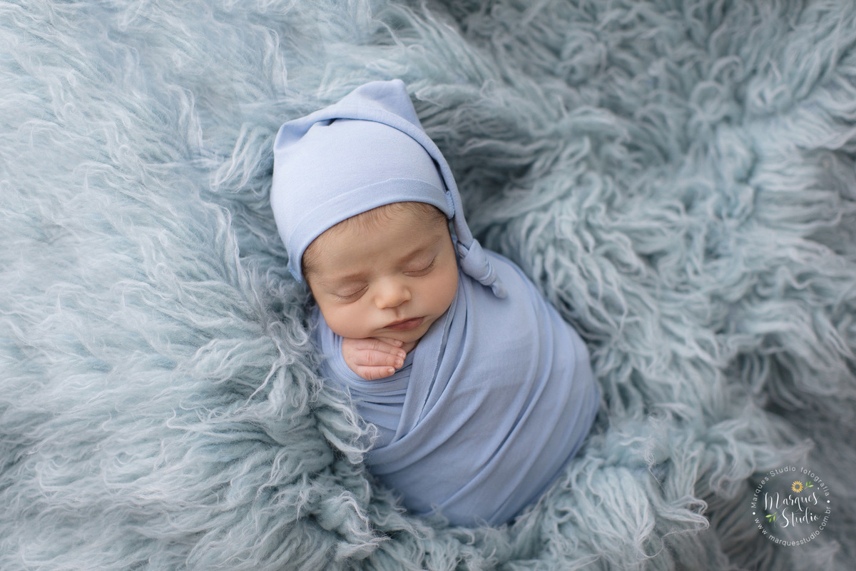 Foto feita para ensaio fotografico de Newborn do Gabriel. Na foto temos o recém nascido enrolado em um wrep azul claro, deitado em um tapete da mesma cor, usando um gorro também azul. O studio esta localizado em Perdizes - São Paulo, SP.