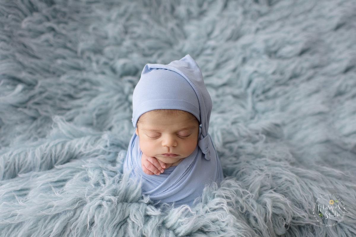 Ensaio fotografico de Newborn do Gabriel. Na foto temos o recém nascido enrolado em um wrep azul claro como um saco de batatas em um tapete da mesma cor, ele usa um gorro também azul claro. O studio encontra-se localizado na Zona Oeste de São Paulo, SP.