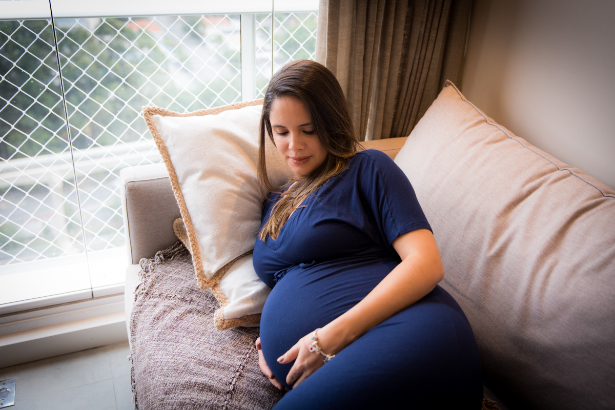 gestante olhando sua barriga de 9 meses em foto feita em sua casa em SP
