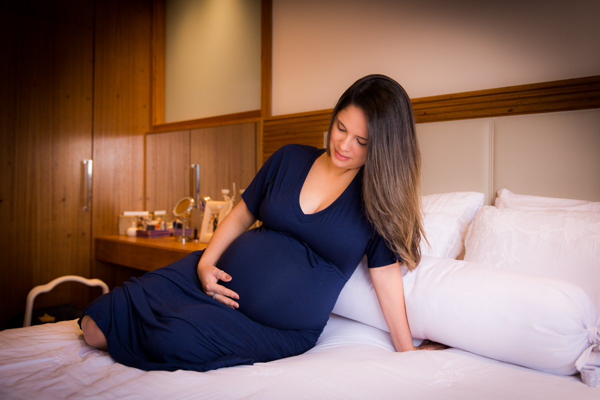 gestante admirando sua barriga de 9 meses em foto feita em sua casa em SP