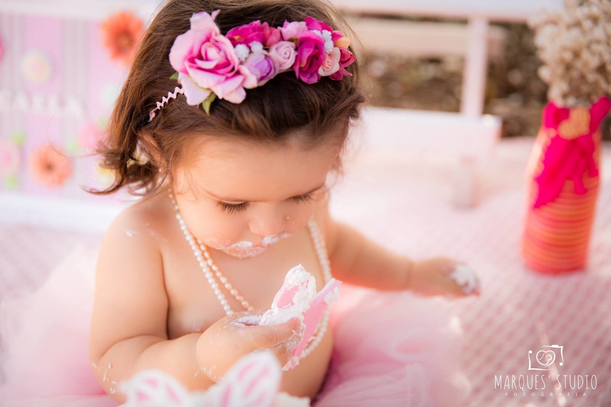 menina esmagando o bolo com roupinha rosa e headband