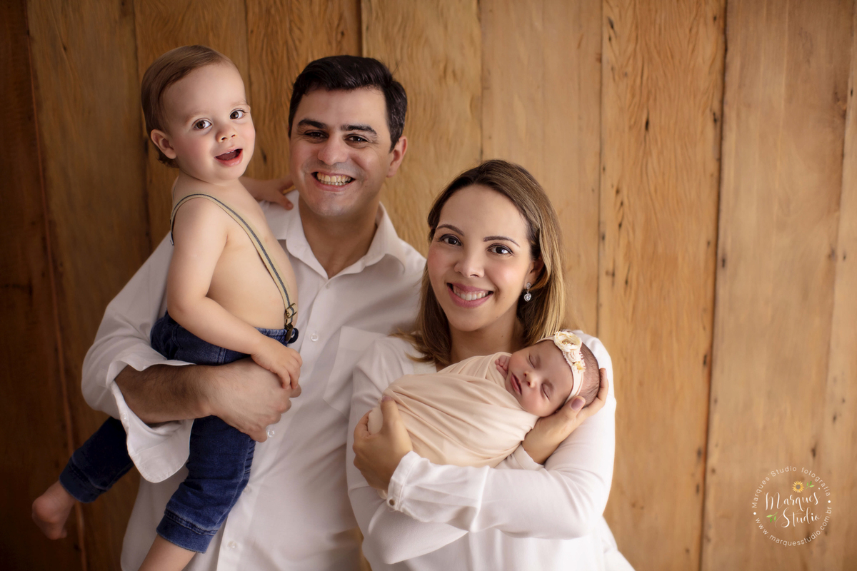 Fotografia tirada no ensaio newborn da Laura de 11 dias. Na foto a bebê está enrolada em um wrap salmão e está no colo da sua mamãe enquanto o papai segura seu irmãozinho do lado. O studio encontra-se localizado em Sumaré - São Paulo, SP