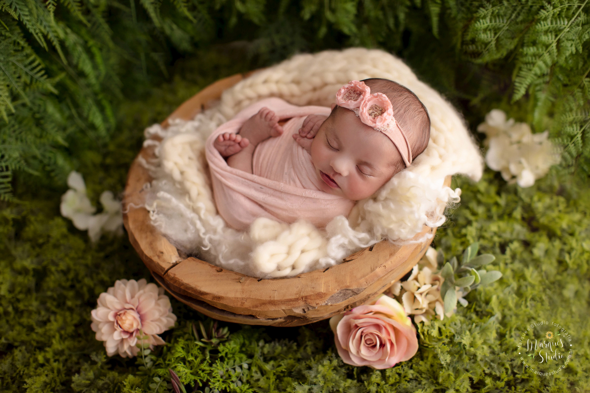 Fotografia registrada no ensaio newborn da Laura de 11 dias. Na foto a Laura está enrolada em um wrap rosa, em cima de uma bacia de madeira e o fundo fotográfico é um lindo jardim. O studio encontra-se em Osasco - São Paulo, SP.