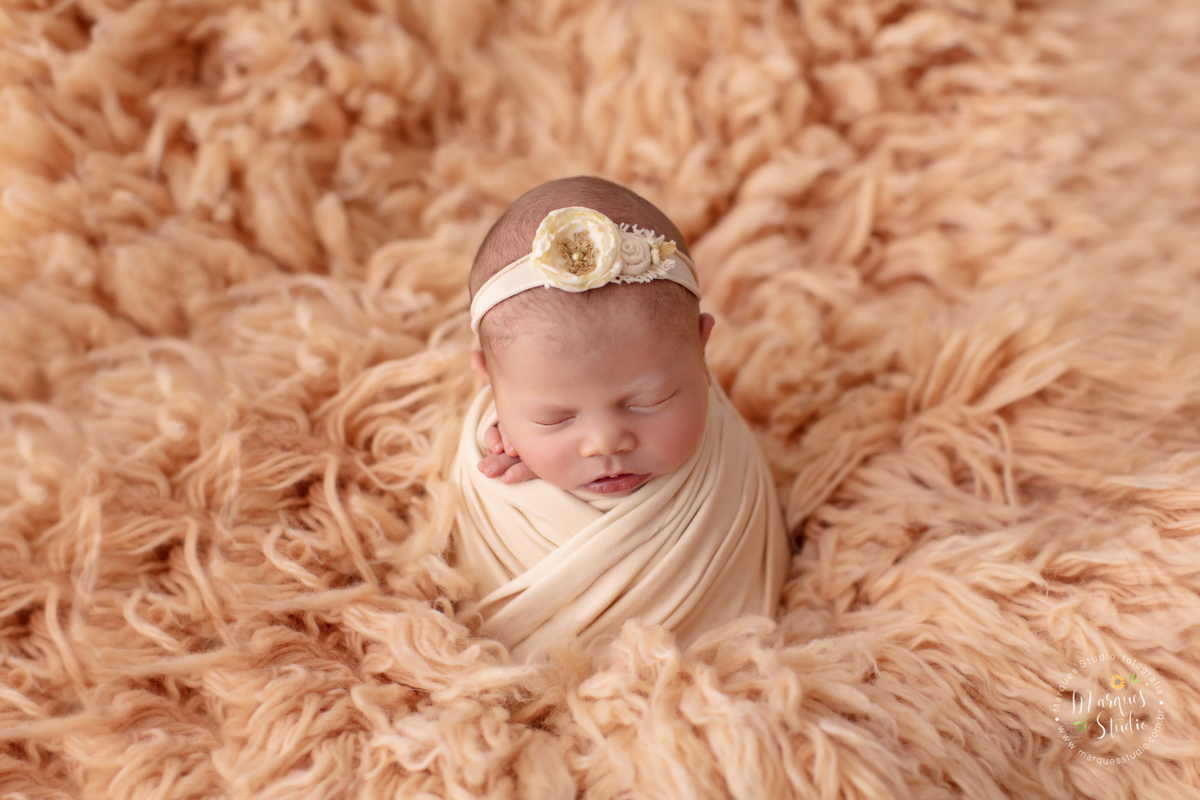Fotografia feita para o newborn da Alice de 18 dias. Na foto a bebê está enrolada em um wrep salmão, em cima de um tapete também salmão, usando uma tiara na cabeça. A foto foi feita no studio que fica localizado em Sumaré - São Paulo, SP. 