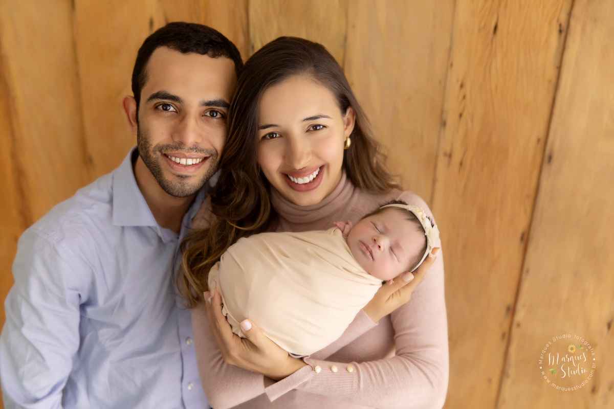 Foto registrada da família da Manuela em seu ensaio Newborn em studio localizado Vila Madalena - São Paulo. Na foto a Manuela está no colo da sua mamãe enquanto o papai abraça as duas. Eles estão sorrindo e felizes.