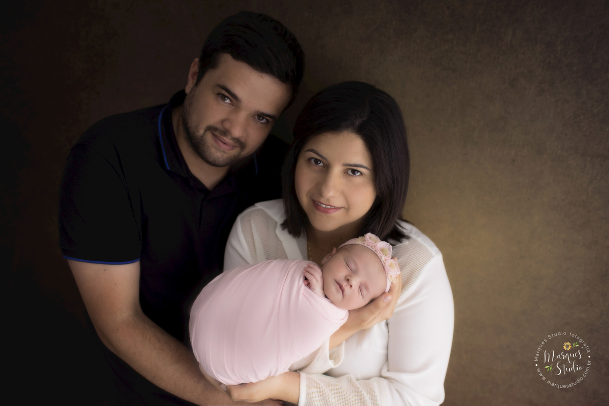 Ensaio newborn da Laura, na foto a mamãe está segurando a sua bebê, enquanto o papai abraça as duas. A Laura está enrolada em um wrep rosa. O studio fica localizado no Itaim Bibi - São Paulo, SP.