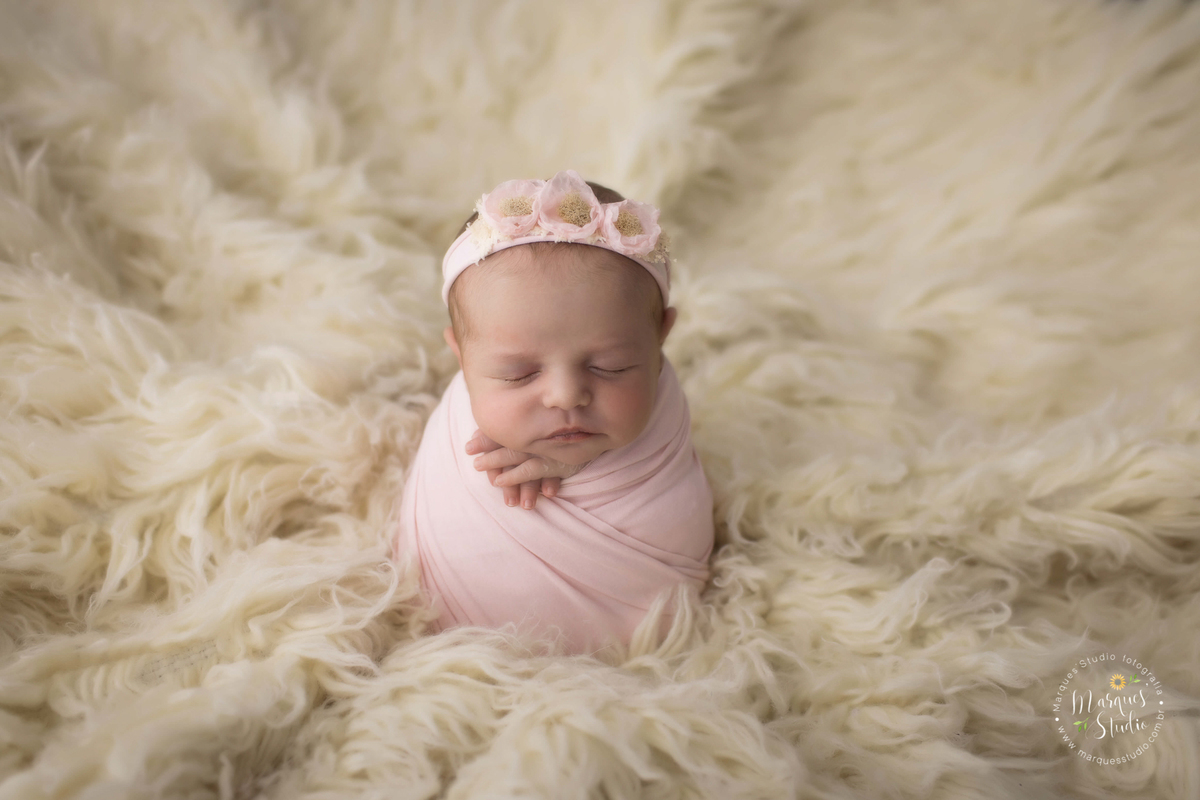 Foto registrada no ensaio newborn da Laura de 14 dias. Na foto ela está  enrolada em um rep rosa, usando uma tiara rosa, em cima de um tapete bege. O studio fica localizado na Av. Consolação - São Paulo, SP.