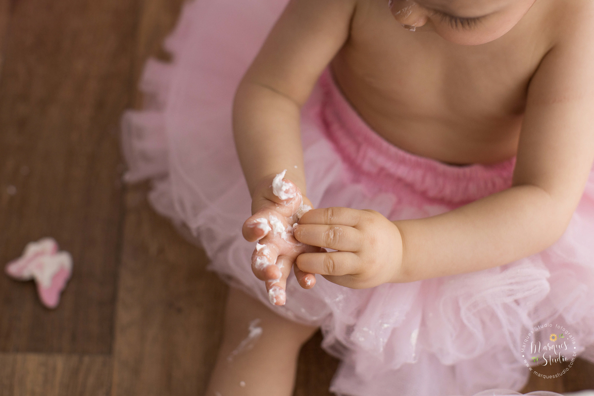 Ensaio Smash the cake da Lais em studio encontrado na Zona Sul de São Paulo, SP. Na foto temos um close nas mãozinhas sujas de bolo da Lais. 