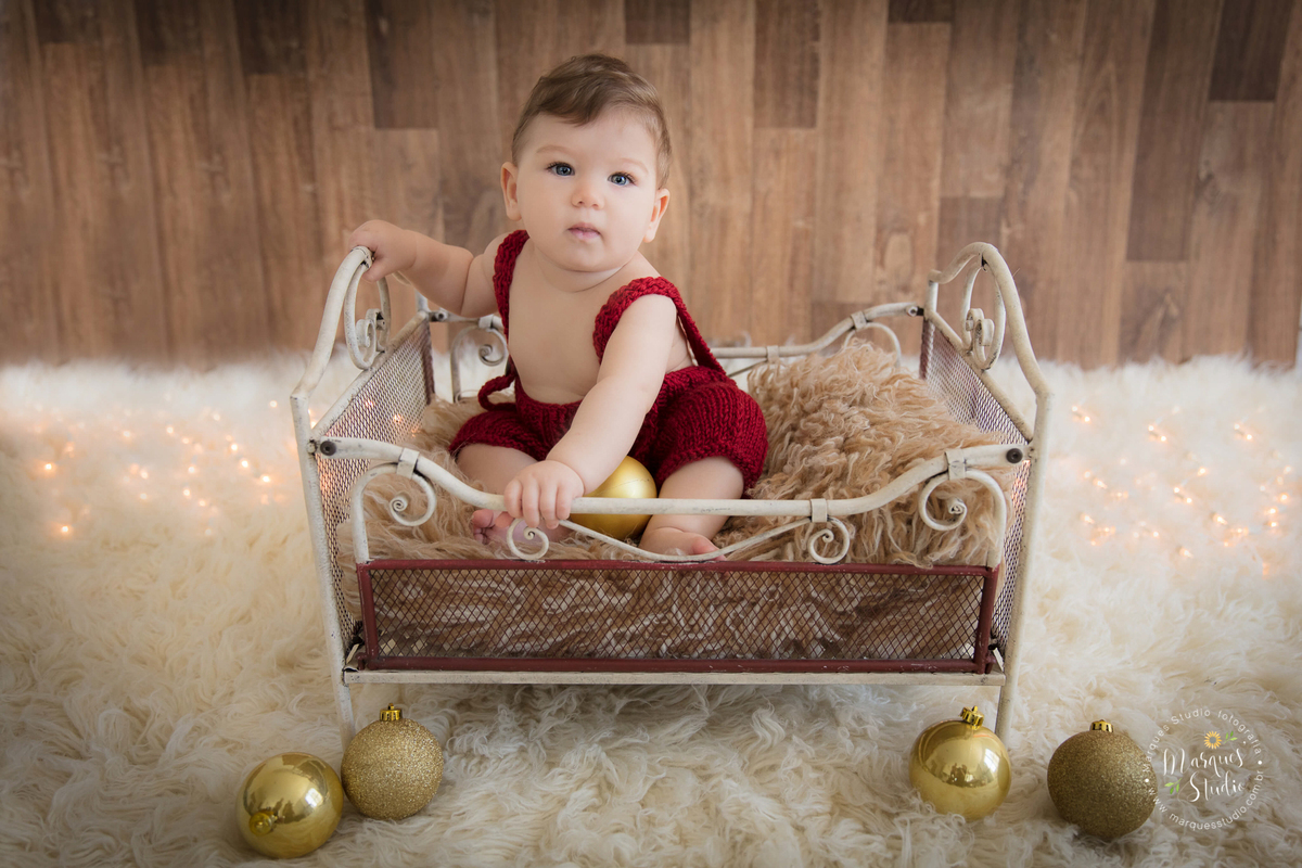 Foto feita em ensaio de bebê do Leonardo em studio localizado na Av Consolação- São Paulo, SP. Na foto o bebê está sentado em um berço bege, usando um lindo macacão vermelho de crochê.