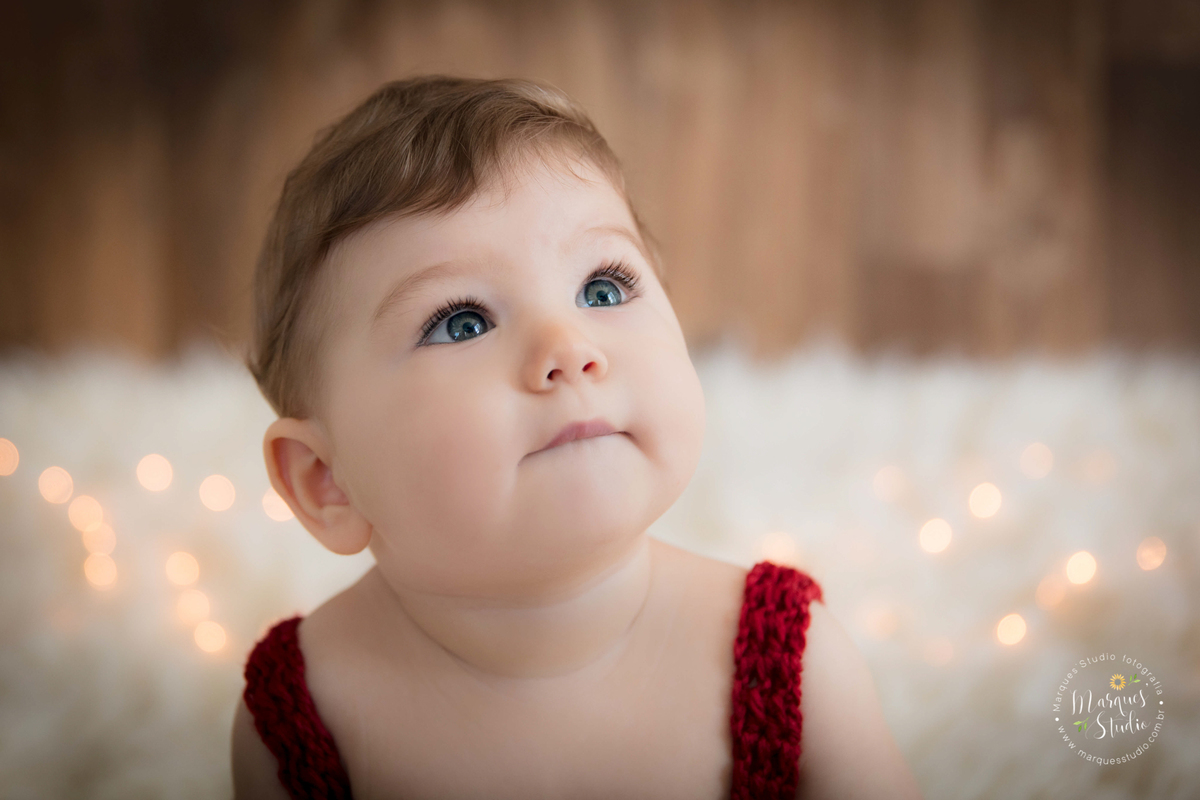 Foto feita em ensaio de bebê do Leonardo em studio localizado na Av Paulista - São Paulo, SP. Na foto o bebê está sentado em um berço bege, usando um lindo macacão vermelho de crochê, a foto é um lindo close no rosto do bebê que está pensativo