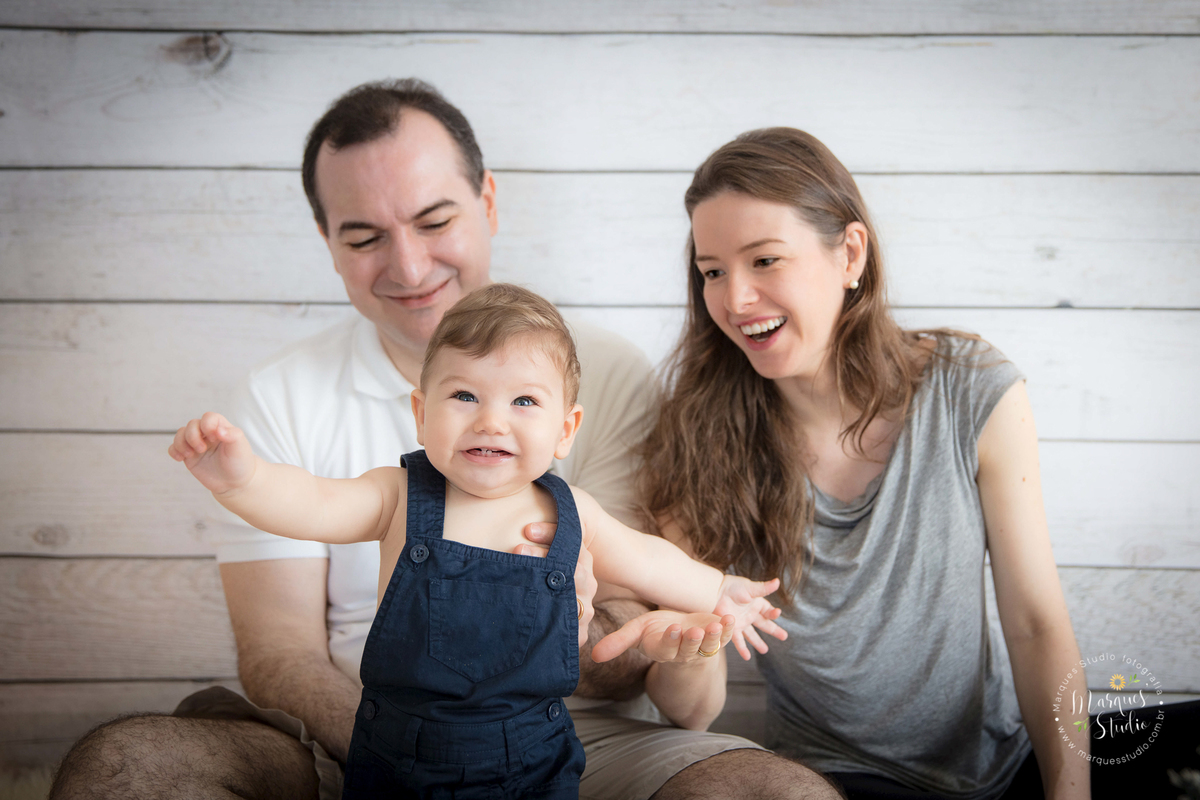 Foto da familia do Leonardo no seu ensaio de acompanhamento com 6 meses. Na foto o bebê está andando e o papai e a mamãe estão segurando e rindo com ele. Studio localizado na Av. Brigadeiro - São Paulo, SP