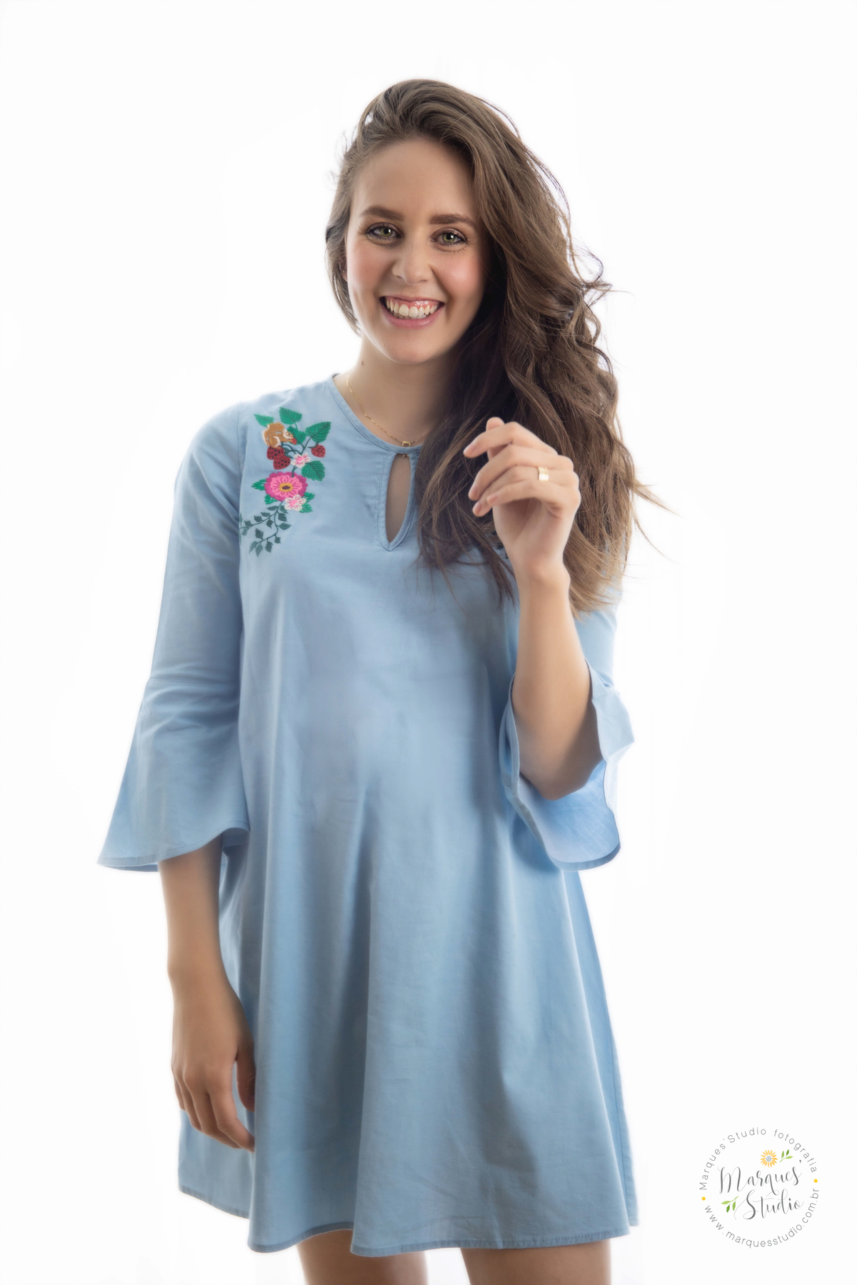 Fotografia registrada no ensaio de familia da Nicoly e do Dante, em studio que encontra-se localizado em Santo Amaro - São Paulo, SP. Na foto a Nioly está em pé usando um lindo vestido azul, ela está sorrindo e com um braço próximo ao rosto. 