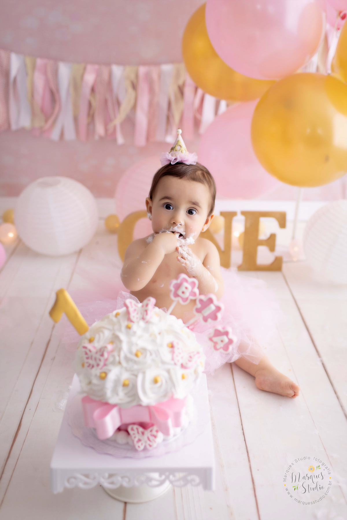 Ensaio Smash the cake da Bia de um ano feito em studio fica localizado em Santo Amaro - São Paulo, SP. Na foto temos a Bia comendo bolo com as mãos bem sujas e um sorrisinho sapeca no rosto.