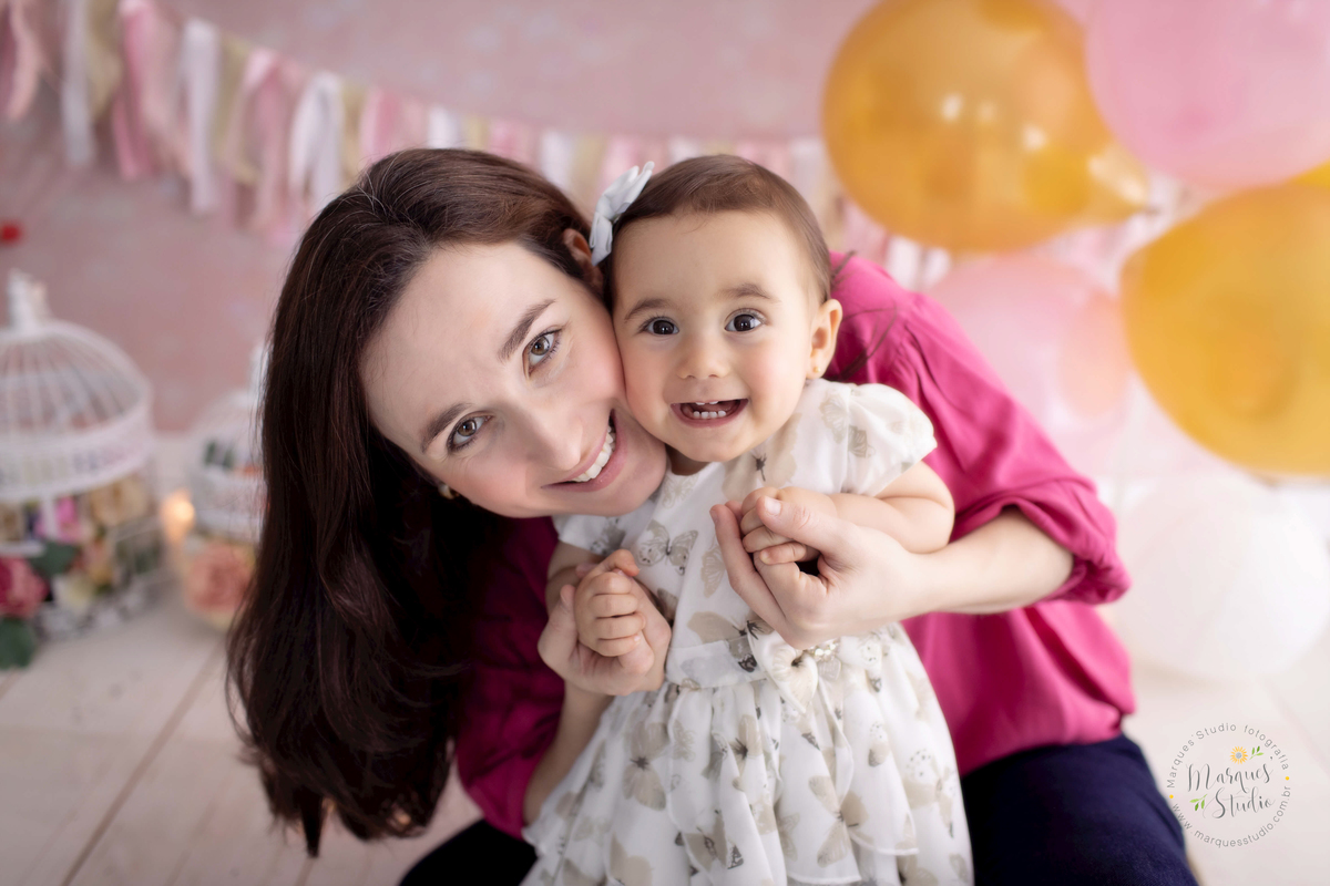 Ensaio Smash the cake da Bia de um ano feito em studio fica localizado na Oscar Freire - São Paulo, SP. Na foto temos a Bia sendo abraçada pela sua mamãe. As duas estão sorridentes e felizes