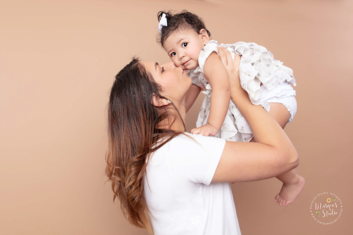 Fotografia feita no ensaio smash the cake da Marina de 1 ano. Na foto a bebê está sendo jogada pra cima por sua mamãe enquanto recebe um beijo dela. O studio localiza-se na Av. Consolação - São Paulo, SP 