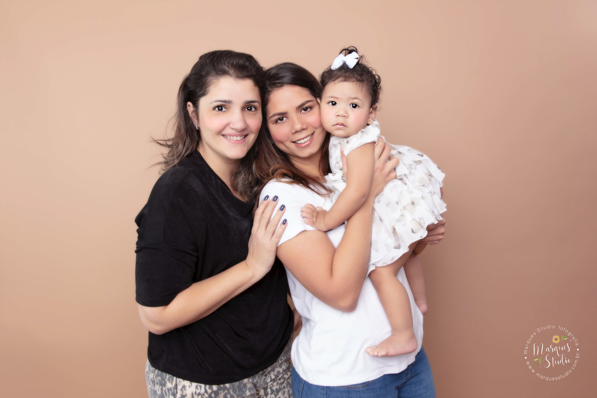 Fotografia feita no ensaio smash the cake da Marina de 1 ano. Na foto a bebê está no colo da sua mamãe enquanto recebe um abraço da mamãe e da madrinha. O studio encontra-se na Vila Madalena - São Paulo, SP. 