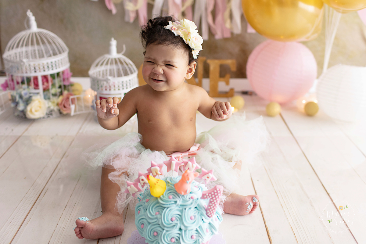 Ensaio feito em studio localizado na Vila Madalena - São Paulo, SP. Na foto temos a Marina no seu smash the cake. A bebê está usando uma tiara de flores no cabelo, está com as mãos sujas de bolo, ela esta sorrindo e se divertindo com o seu bolo