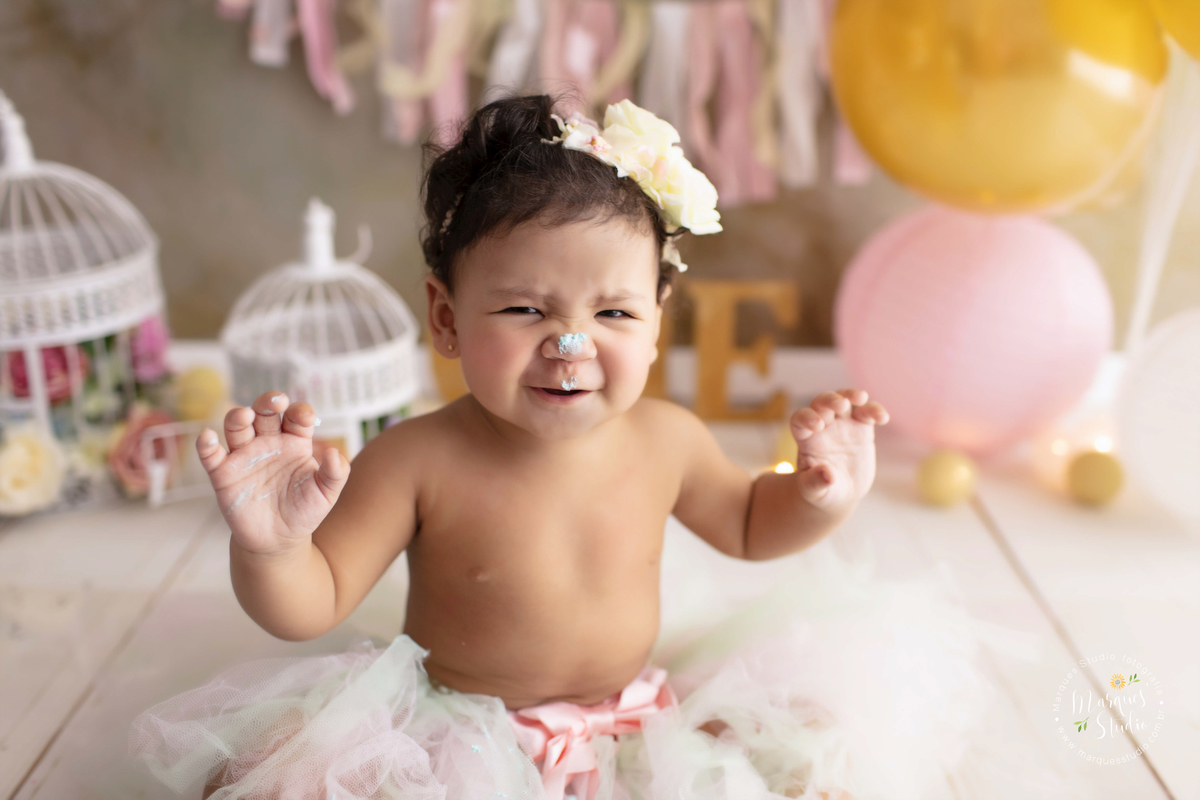 Foto realizada em studio localizado em Perdizes - São Paulo, SP, na foto temos a Marina no seu smash the cake. Um close do rosto do bebê que está com as mãos e o nariz sujo de bolo, sorrindo e se divertindo com sua sujeira.