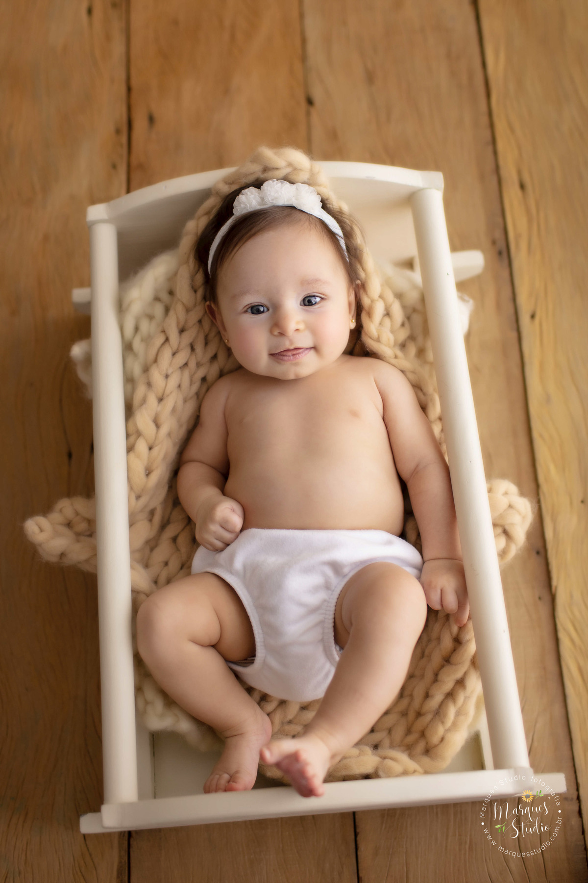 Ensaio feito em studio localizado em Perdizes - São Paulo, SP. Na foto a Manuela de 3 anos está deitada em berço branco, usando uma calcinha branca e um lacinho na cabeça. A foto mostra todo o corpo do bebê que está sorrindo para a foto