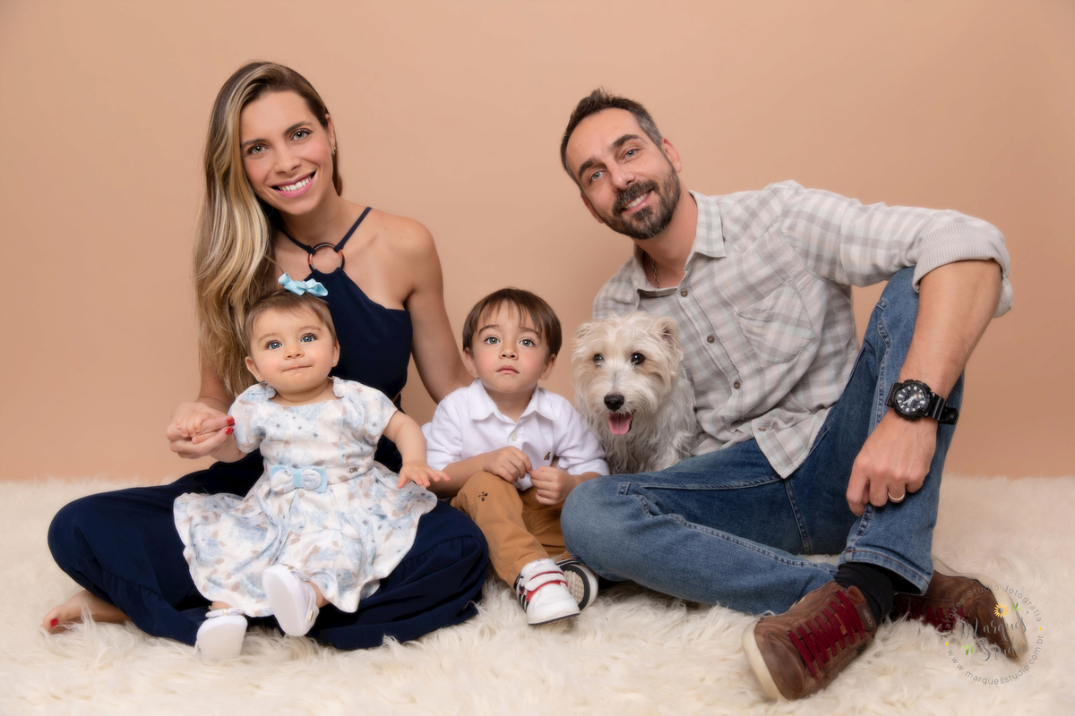 Foto da família da  Giovanna de 7 meses, feito em seu ensaio de acompanhamento em studio localizado no Bela Vista - São Paulo, SP. Na foto a Giovanna está sentada no colo da mamãe, seu irmãozinho está do lado e o papai está segurando o cachorro da família