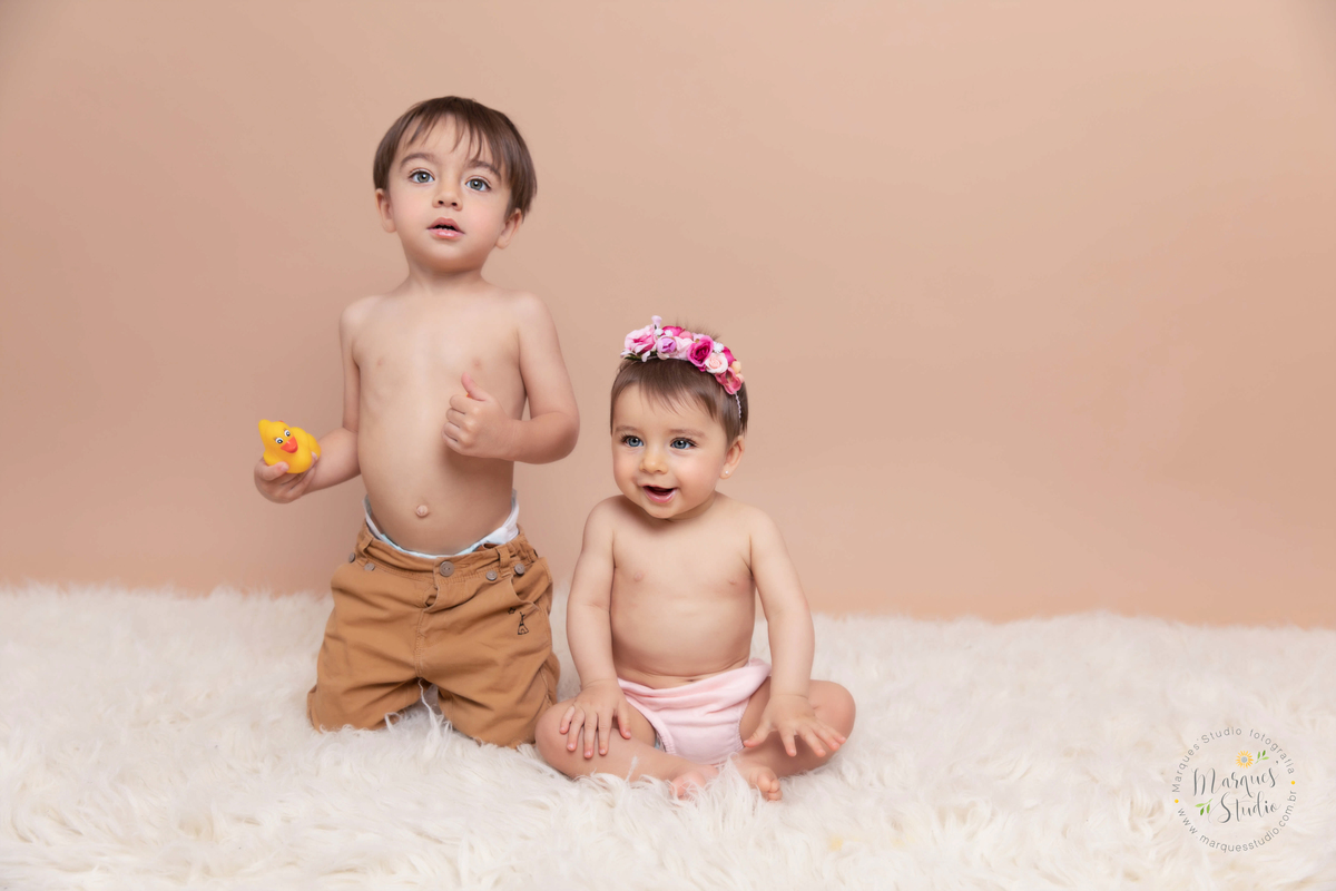 Foto da Giovanna de 7 meses, feito em seu ensaio de acompanhamento em studio localizado no Morumbi  - São Paulo, SP. Na foto a Giovanna está sentada em um tapete branco junto com o seu irmão mais velho, os dois estão sorridentes
