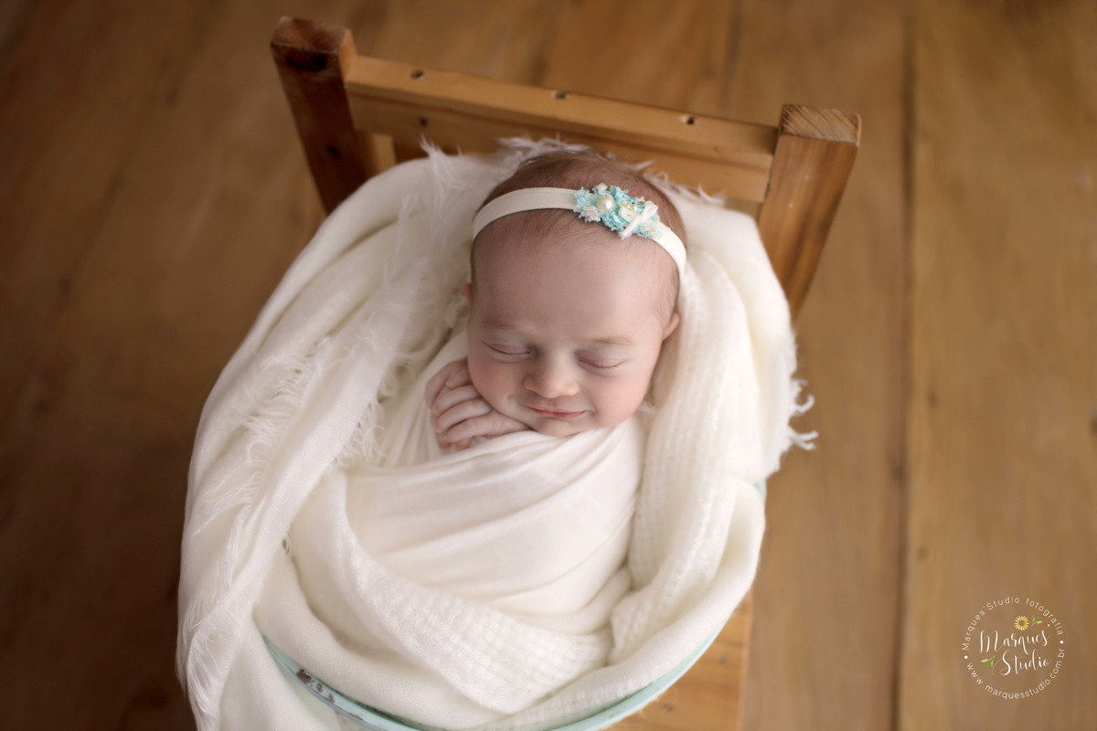 Foto feita para ensaio newborn em studio localizado em Santo Amaro - São Paulo, SP. Na foto a bebê está enrolada em um wrep branco e está dentro de um balde azul. 