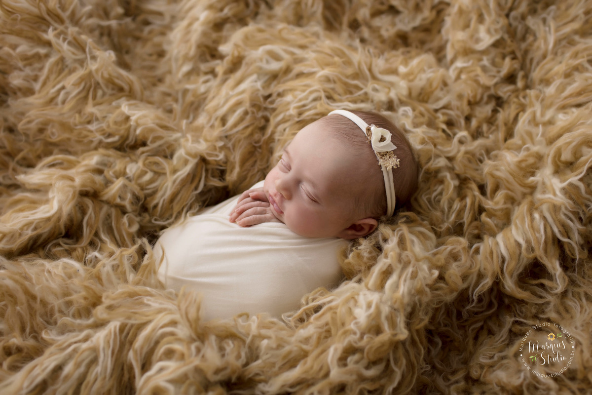Fotografia feita em studio localizado na Av. Paulista - São Paulo, SP. Na foto a bebê está enrolada em um wrep branco em cima de um tapete mesclado.