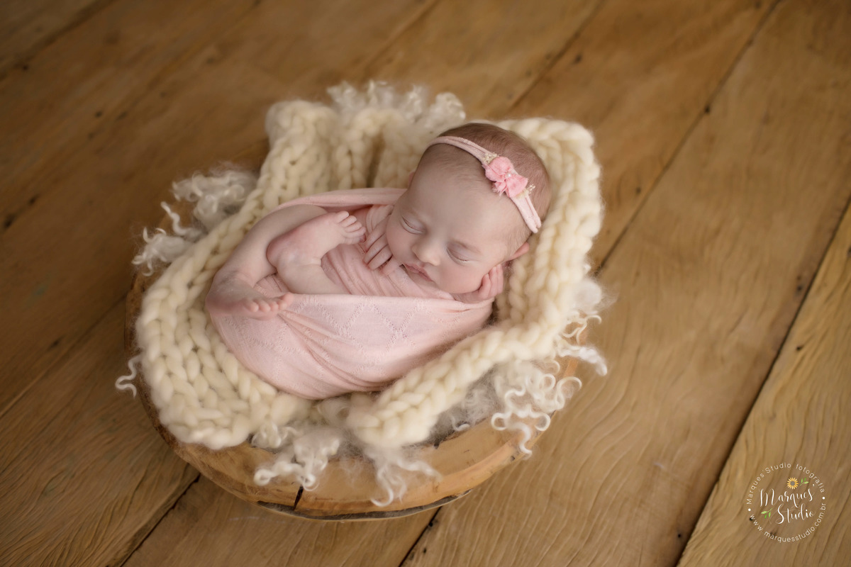 Foto feita para ensaio newborn em studio localizado em Osasco  - São Paulo, SP. Na foto a bebê está enrolada em um wrep rosa e está dentro de um crop de madeira com pelos brancos. 