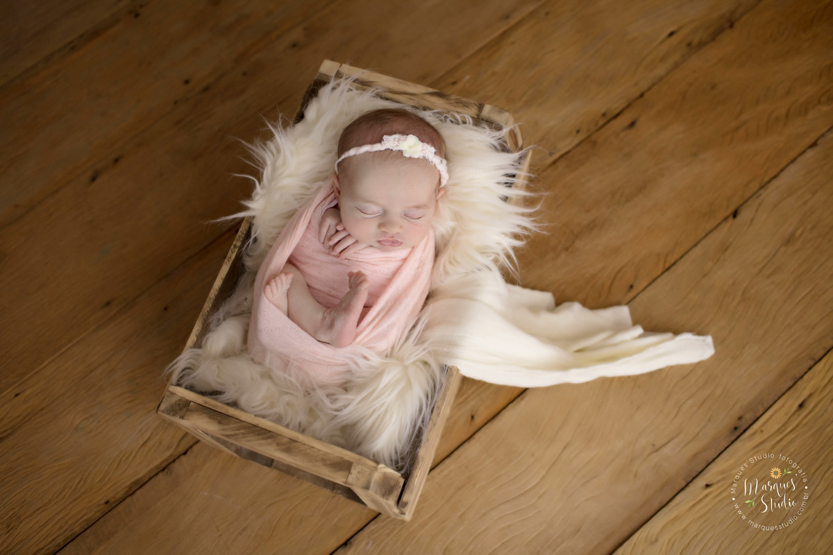 Foto feita para ensaio newborn em studio localizado em Santo Amaro - São Paulo, SP. Na foto a bebê está enrolada em um wrep rosa e está dentro de um baú de madeira com pelos brancos. 