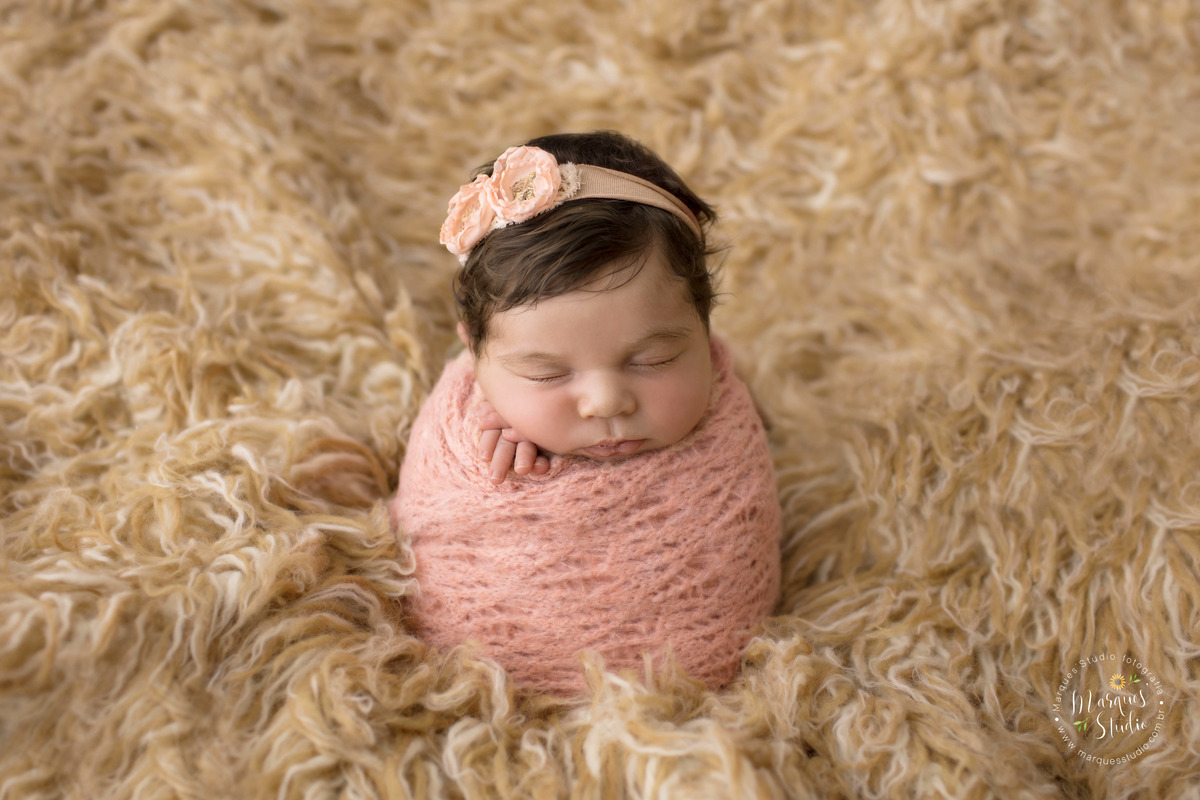 Fotografia feita em studio localizado na Av. Paulista - São Paulo, SP. Na foto a bebê está enrolada em um wrep de tricô rosa em cima de um tapete mesclado.
