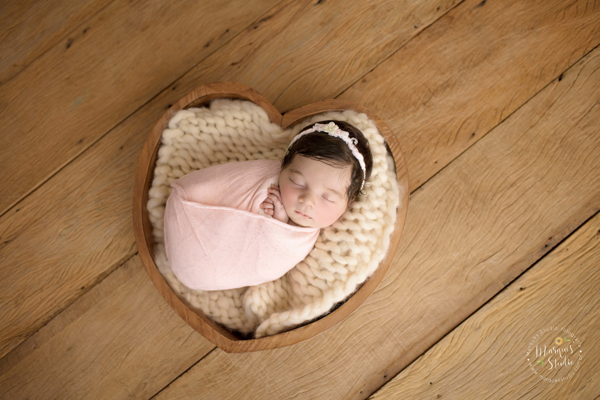 Foto feita para ensaio newborn em studio localizado em Sumaré - São Paulo, SP. Na foto a bebê está enrolada em um wrep rosa e está dentro de um crop em formato de coração.