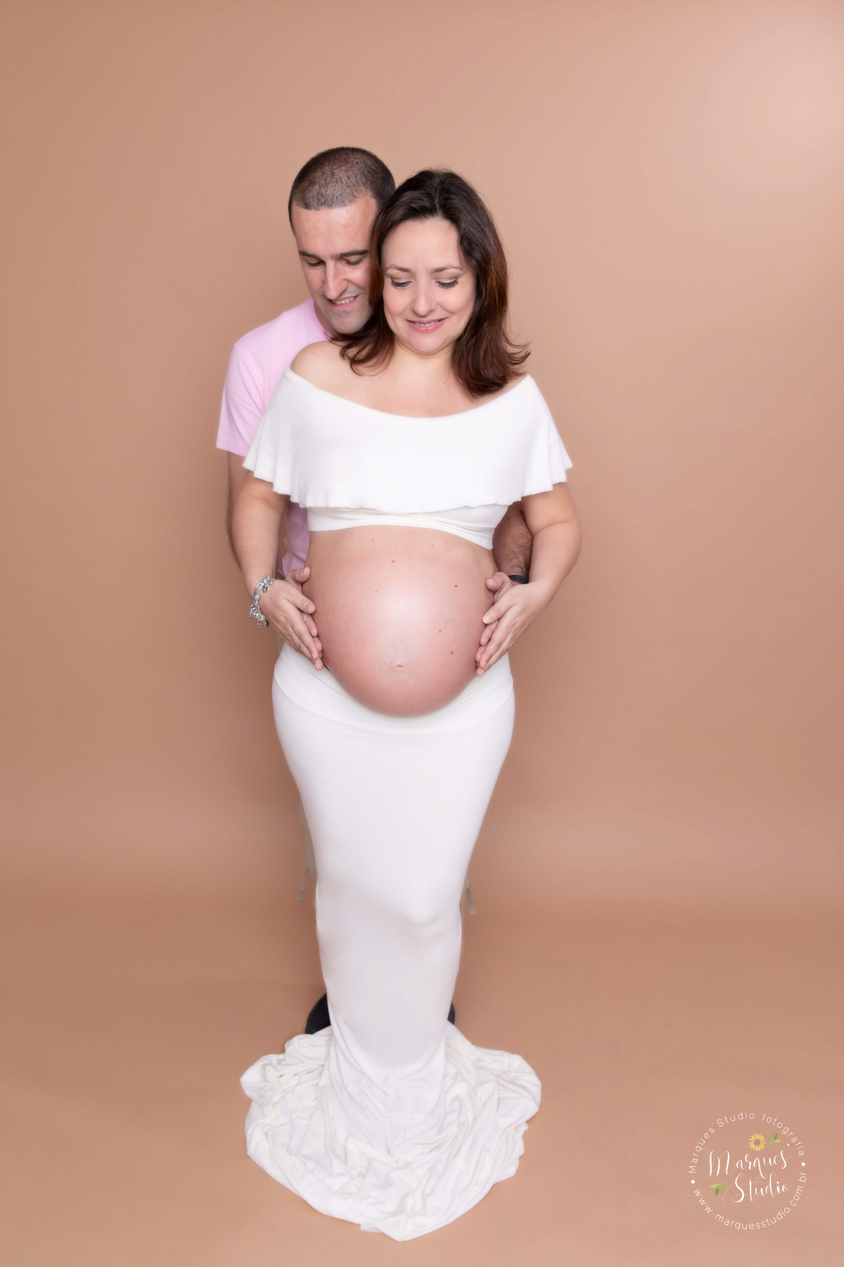 Ensaio fotografico realizado em studio localizado na Vila Prudente - São Paulo, SP. Na foto a mamãe está usando um conjunto de saia e top no branco, enquanto seu marido a abraça por trás
