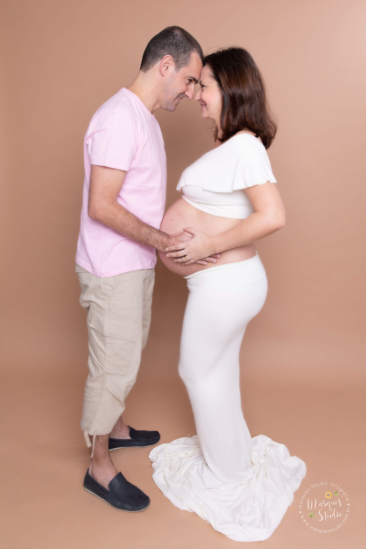 Ensaio fotografico realizado em studio localizado na Anália Franco - São Paulo, SP. Na foto a mamãe está usando um conjunto de saia e top no branco, ela e o marido estão com as mãos na barriga e de frente um para o outro