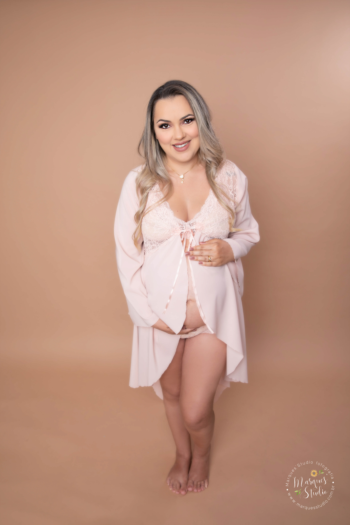 Ensaio de gestante realizado em studio localizado no Bela Vista - São Paulo, SP. Na foto a mamãe está usando uma camisola rosa, com as mãos na barriga e dando um lindo sorriso para o seu bebê