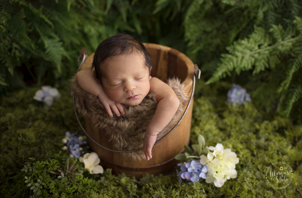 Foto feita para ensaio newborn do Pietro de 12 dias, em studio localizado no Jardins - São Paulo, SP. Na foto o bebê está dentro de baldinho de madeira com o fundo fotográfico de um lindo jardim verde e florido