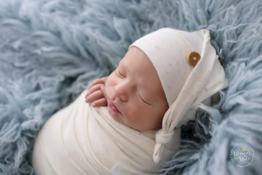 Foto feita para ensaio newborn do Pietro de 12 dias, em studio localizado em Perdizes - São Paulo, SP. Na foto o bebê está deitado em um tapete azul claro enrolado em um wrep branco como um saquinho de batatas. 
