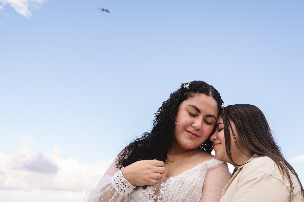 Ensaio de pré casamento casal sentido o toque e a emoção de estarem juntas na natureza com o céu azulado