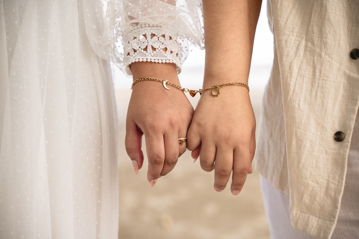 Ensaio de pré casamento na praia, detalhe de mão com dedo mindinho entrelaçados dando detalhe a pulseira do casal que tem grande significado