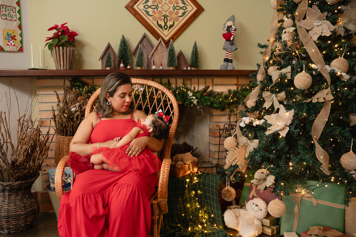 Ensaio de natal, natal 2024, ensaio de família, mãe amamentando a filha ao lado da árvore de natal