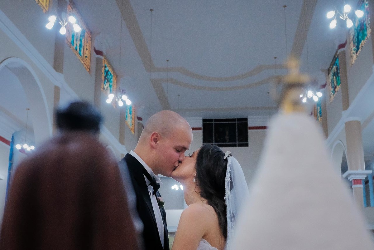 o momento do beijo visto entre as imagens de Nossa Senhora Aparecida e São Benedito em cerimônia de casamento em Guaratinguetá foto erasmo ballot