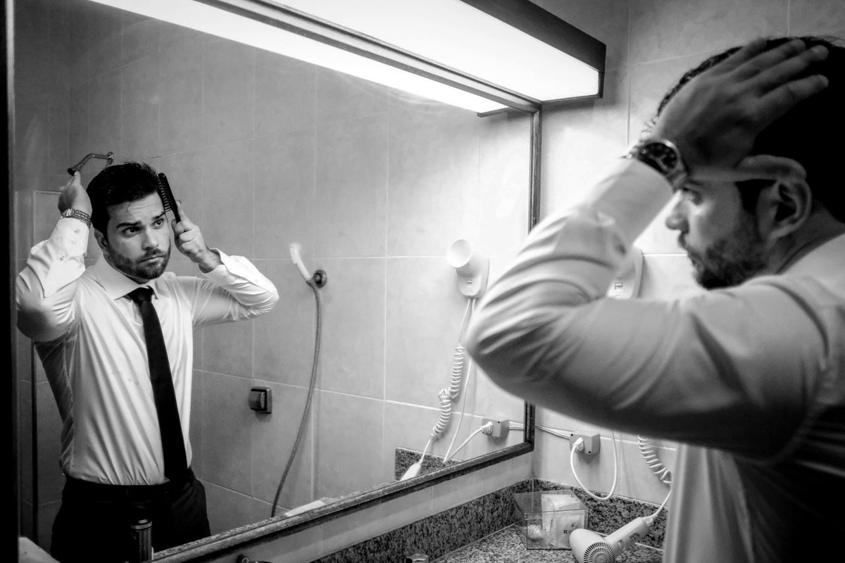 noivo se arruma ansioso prepara penteado se vendo no espelho um pouco nervoso em casamento lindo no pôr do sol no hotel fazenda sete lagos em Guaratingueta fotos erasmo ballot