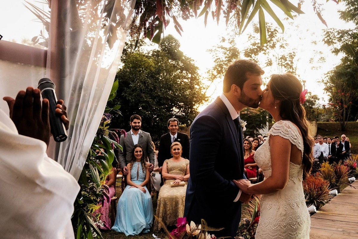 noivos se beijam e convidados observam o lindo beijo e se emocionam com o casal feliz em casamento lindo no pôr do sol no hotel fazenda sete lagos em Guaratinguetá fotos erasmo ballot